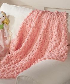 a pink crocheted blanket sitting on top of a white couch