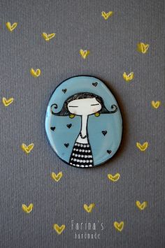 a button with a woman's head in the center on a gray surface surrounded by small yellow hearts