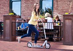 a woman is riding an electric scooter in front of a restaurant with people sitting at tables