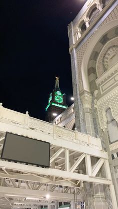 the clock tower is lit up in green and white at night, as seen from below