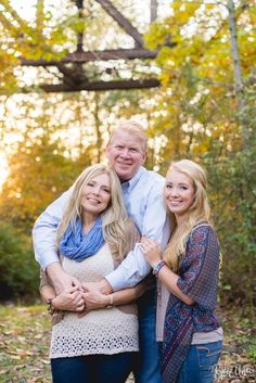 an older man and two young women posing for a photo in front of some trees