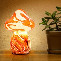 an orange and white lamp sitting on top of a table next to a potted plant