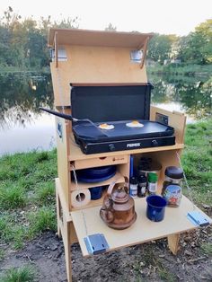 an outdoor grill is set up next to the water with other camping items on it