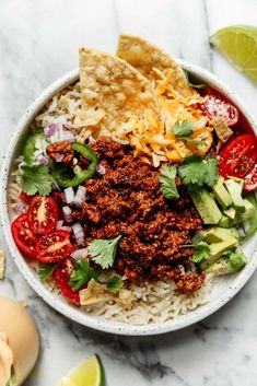 a bowl filled with rice, meat and veggies next to tortilla chips