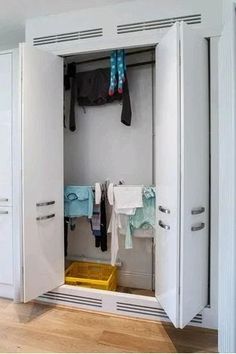 an open white closet with clothes hanging on the rack and two yellow bins next to it