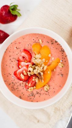 a white bowl filled with fruit on top of a table next to sliced strawberries