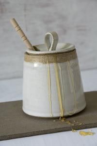 a white ceramic container with a wooden spoon in it and some yellow paint on the inside