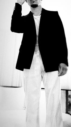 a man standing in front of a mirror wearing white pants and a black blazer