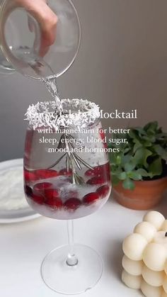 someone is pouring something into a wine glass with ice and cranberries in it