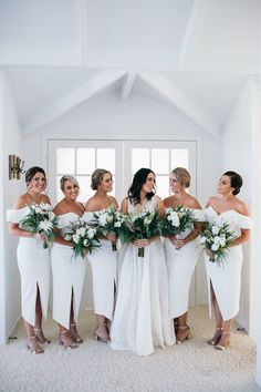 a group of women standing next to each other in front of a white wall with flowers