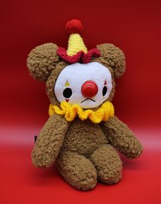 a brown teddy bear with a clown hat on it's head and nose sitting in front of a red background