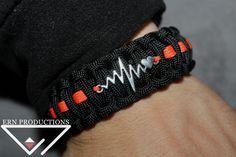 a person wearing a black bracelet with an orange and white heartbeat on it