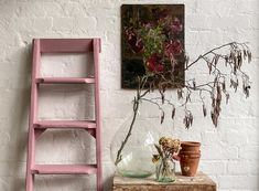 two vases with flowers are sitting on a table next to a pink shelf and ladder