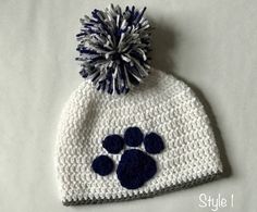 a crocheted hat with a blue and white paw print on the front has a pom - pom attached to it