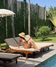 a woman sitting on top of a wooden deck next to a pool with an umbrella