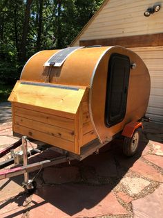 a small trailer with a wooden structure on the back and side wheels is parked in front of a house