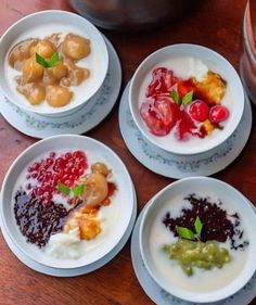 four white plates topped with different types of food on top of a wooden table next to a pot