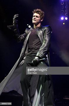 a man in black leather jacket and gloves on stage with his hands out to the side