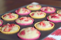 cupcakes with white frosting and strawberries in them on a baking tray