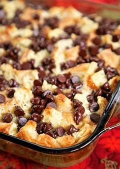 a casserole dish with chocolate chips and bread in it on a red tablecloth