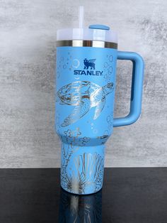 a blue tumbler cup with a sea turtle on the front and bottom is sitting on a table