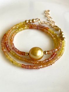 Petite sapphires, 2-4mm, ranging in color from yellow to peach, orange, and red, frame a gorgeous 10mm gold South Sea pearl.   The golden color is intense! Necklace measures 16" with 14K gold-filled findings, and comes with a 2" gold-filled extender chain to bring it to 18".  Works great as a versatile layering piece, or shines all on its own.   Your jewelry will come gift-boxed, and gift-wrapping is available upon request.  Thanks for checking out my shop! Elegant Gold Round Bead Gemstones, Yellow Gemstone Round Beads Jewelry, Yellow Gemstone Jewelry With Round Beads, High Luster Yellow Gold Pearl Necklace With Round Beads, Elegant Gold Gemstones With Gemstone Beads, Elegant Gold Gemstones With Beads, Gold Gemstone Beads For Jewelry Making, Gold Briolette Gemstone Pearl Necklace, Gold Single Strand Gemstones As Gift