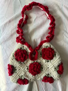 a crocheted purse with red flowers on the front and bottom, sitting on a white sheet