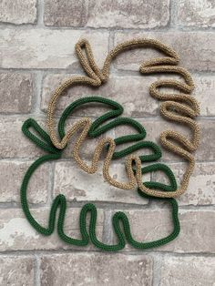 three green and gold roped objects are on a brick wall, with the word love spelled in cursive letters