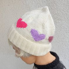 a small child wearing a knitted hat with hearts on it's brim