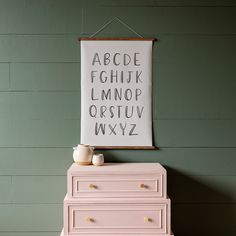 a pink dresser sitting in front of a green wall with a framed poster above it