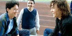 three young men sitting on a tennis court talking to each other and laughing at the same time