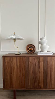 a sideboard with two lamps on top and a lamp next to it in front of a white wall