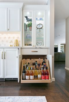 a cabinet filled with lots of bottles of wine in a living room next to a kitchen