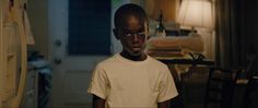 a young boy standing in a living room next to a lamp