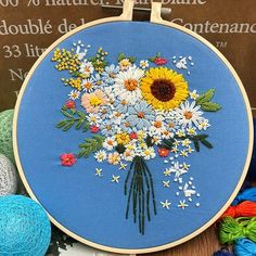 a bouquet of daisies and sunflowers on a blue background is surrounded by balls of yarn