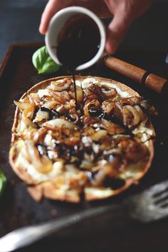 a person is pouring coffee into a pizza on a tray with other food and utensils