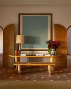 a wooden table with flowers on it in front of a large painting and lamp shade