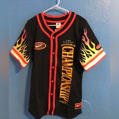 a black baseball jersey with flames on it hanging from a hanger against a blue wall