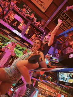 two women are playing video games in a pinball game room while others watch from the stands