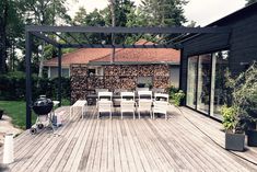 a wooden deck with chairs and grill in the middle of it next to a building