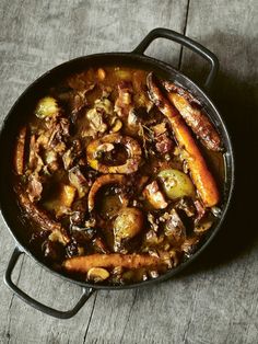 a stew with carrots, potatoes and meat in a pan on a wooden table