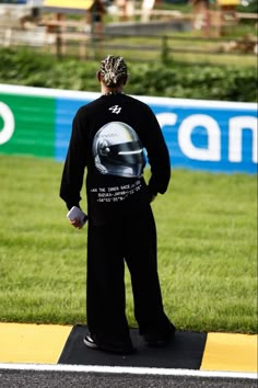 a man standing on the side of a road with a helmet on his shirt and black pants