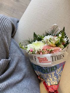 a bouquet of flowers sitting on the back of a couch in front of a gray sweater