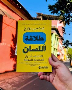 a person holding up a yellow book in front of a red building with arabic writing on it