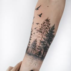 a person's arm with a forest scene tattoo on it and birds flying over the trees