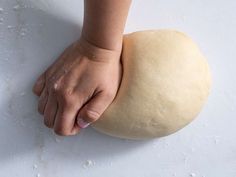 a ball of dough being held by a person's hand on a white surface