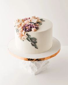 there is a white cake with flowers on the top and gold trimmings around it