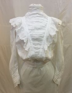 "1890s, 36\" bust, white cotton batiste lace edge blouse ( waist) .  The blouse has pin tucked pleated front, high collar and ruffled yoke.  Sleeves are full mutton chopped with elaborate lace inserts and lace cuffs.  Unfinished bottom meant to be tucked into skirt.  Blouse is fastened in back  with 14 hand crochet buttons.  Hook and eye at top of collar  in back.   Measurements: bust 36\" Waist 26\" Shoulder to shoulder  15\" Shoulder to hem  19\" Sleeves 19\" long Arm holes 7\" Width at bottom Fitted Ruffles Blouse For Gatherings, Fitted Ruffled Blouse For Gatherings, Fitted Ruffle Blouse For Gatherings, Fitted White Blouse With Pintucks, Classic Fitted White Victorian Dress, White Fitted Victorian Blouse, Fitted White Victorian Blouse, White Fitted Classic Victorian Dress, Historical Victorian Dress With Ruffles