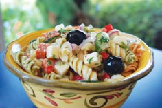 a yellow bowl filled with pasta and olives on top of a blue tablecloth