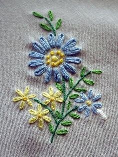 an embroidered piece of cloth with blue and yellow daisies on it, in the shape of flowers